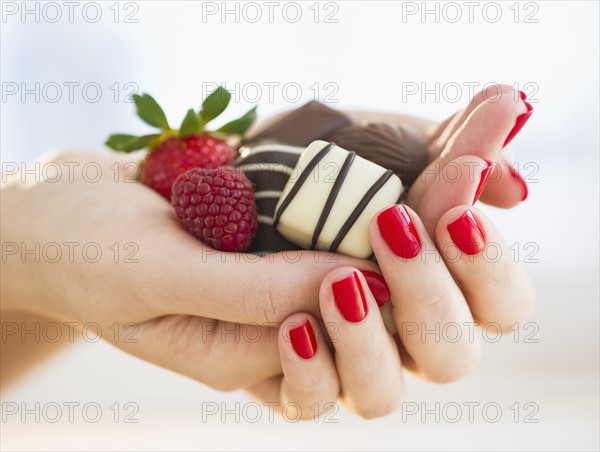 Hand holding chocolates a raspberry and a strawberry.