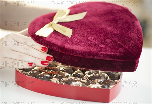 Hand opening a velvet heart shaped box of chocolates.