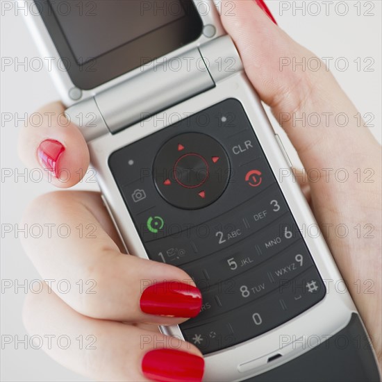 Woman wearing red nail polish holding a cellular phone.