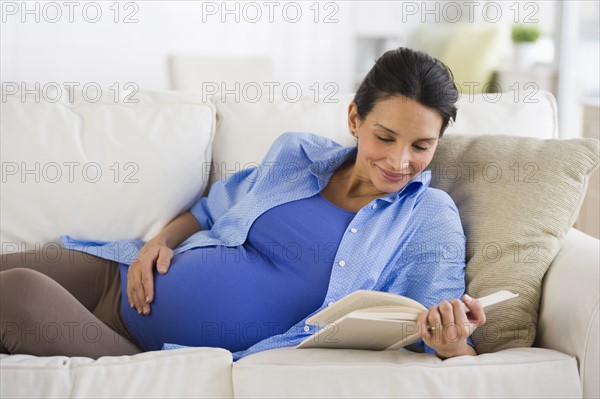 Pregnant woman reading on couch.