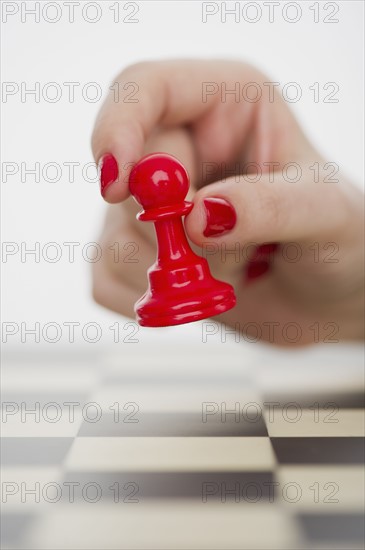 Hand holding red pawn chess piece.