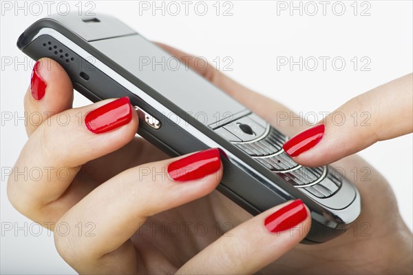Woman wearing red nail polish texting on cell phone.