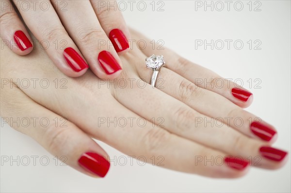 Diamond engagement ring on hands with red nail polish.