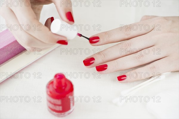 Woman painting her nails with red nail polish.