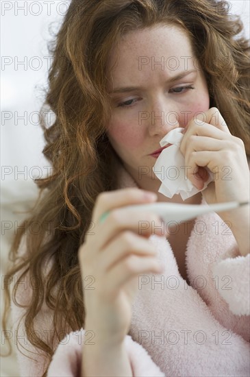 Sick woman looking at thermometer.
