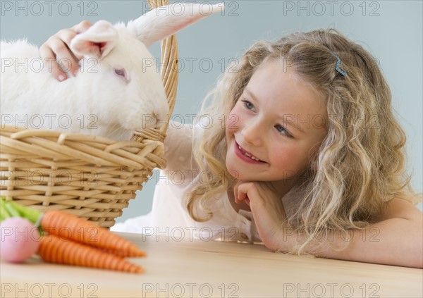 Young girl petting a rabbit in a basket.