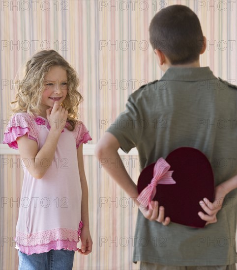 Young boy hiding a box of chocolates from young girl.