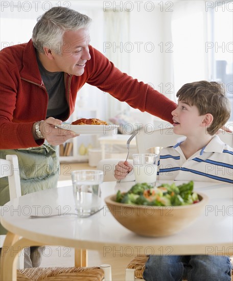 Father giving plate of spaghetti to son. Photographe : Jamie Grill