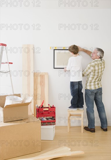 Father and son hanging picture on wall. Photographe : Jamie Grill