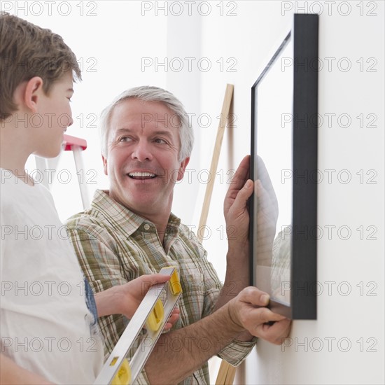 Father and son hanging picture on wall. Photographe : Jamie Grill