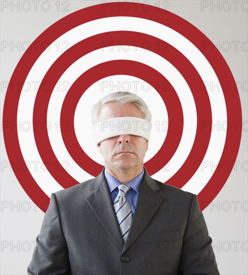 Blindfolded man standing in front of bull's eye. Photographe : Jamie Grill