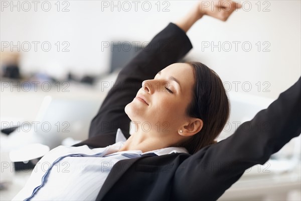 Businesswoman stretching at desk. Photographe : momentimages