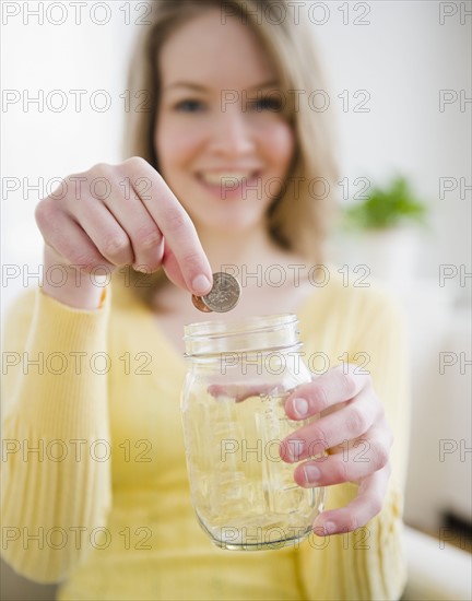 Woman putting coins in a jar. Photographe : Jamie Grill
