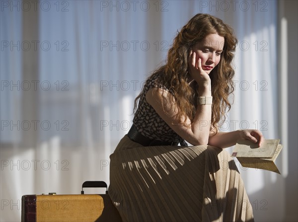 Somber woman sitting on suitcase. Photographe : Daniel Grill