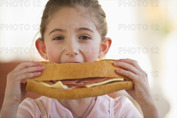 Young girl eating a large sandwich. Photographe : Daniel Grill