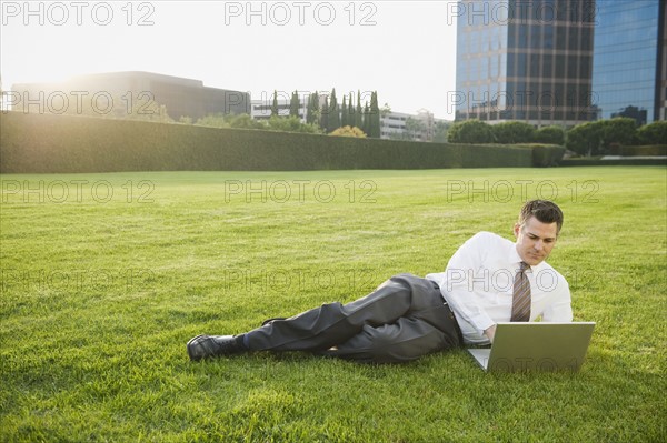 Businessman relaxing with laptop on lawn.