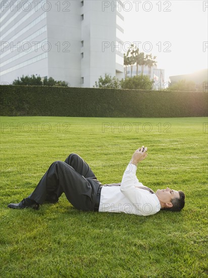 Businessman texting while lying on grass.