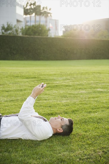 Businessman texting while lying on grass.