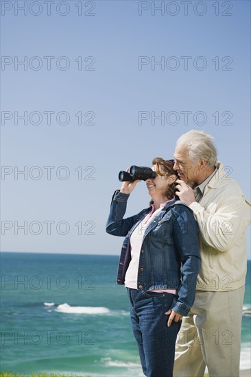 Couple looking at ocean with binoculars.