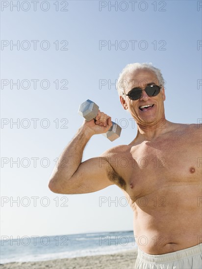 Man exercising with dumbbell on beach.