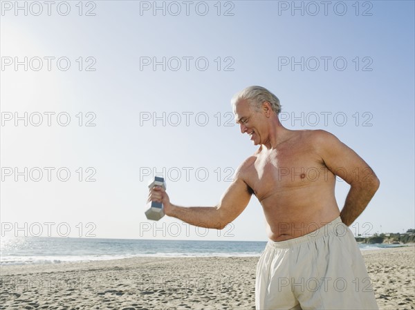 Man exercising with dumbbell on beach.