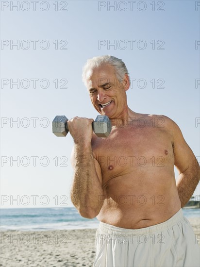 Man exercising with dumbbell on beach.