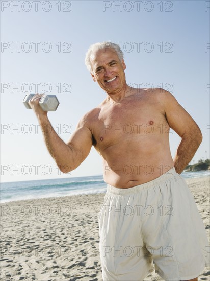 Man exercising with dumbbell on beach.