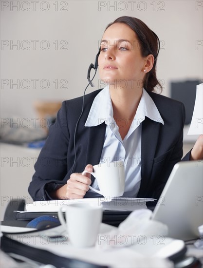 Businesswoman drinking coffee at desk. Photographe : momentimages