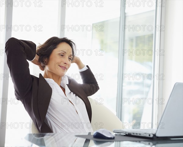 Businesswoman stretching at desk. Photographe : momentimages