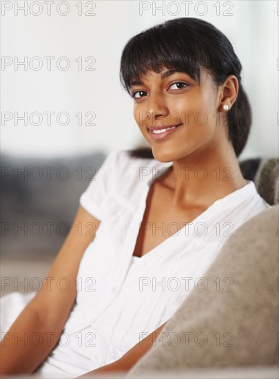 Young woman sitting on couch. Photographe : momentimages
