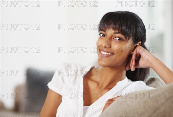 Young woman sitting on couch. Photographe : momentimages