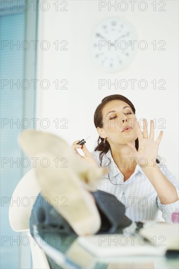 Woman painting fingernails at desk. Photographe : momentimages