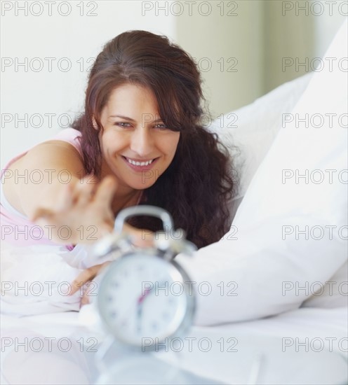 Woman reaching for alarm clock. Photographe : momentimages