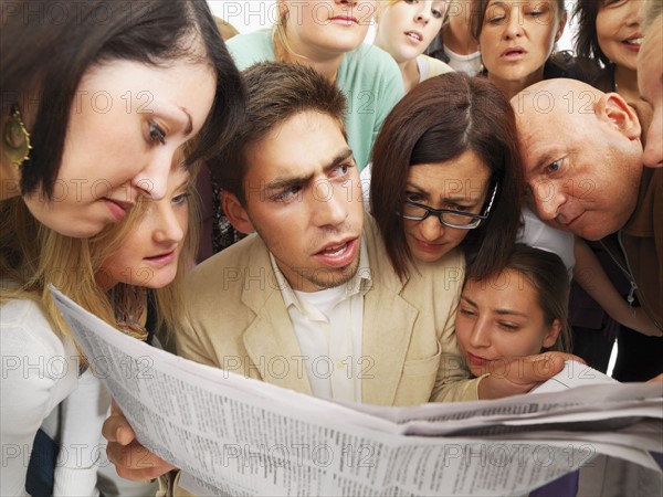 Group of people reading one newspaper. Photographe : momentimages