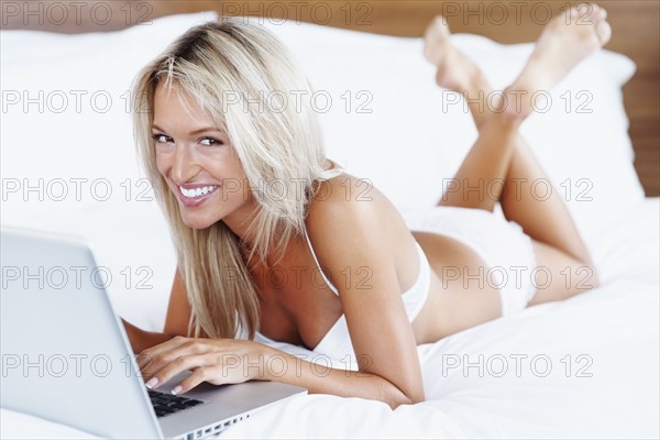 Woman wearing lingerie and typing on laptop. Photographe : momentimages