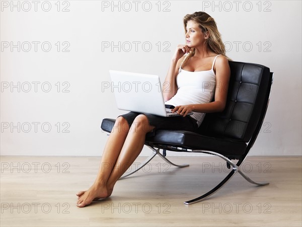 Woman sitting in modern chair while holding laptop. Photographe : momentimages