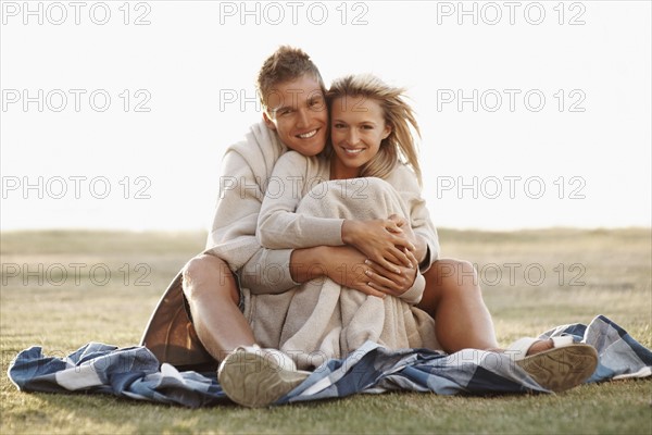 Couple sitting together in a field. Photographe : momentimages