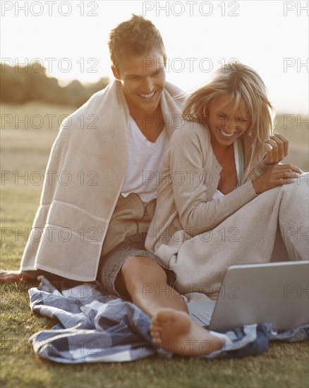 Couple looking at laptop outdoors. Photographe : momentimages