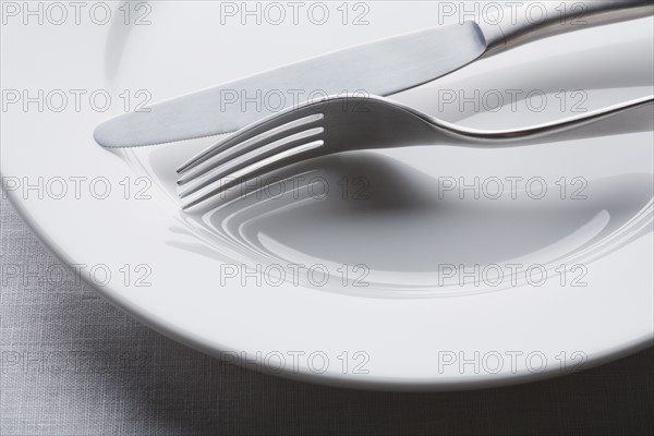 Fork and knife on empty white plate. Photographe : Kristin Lee