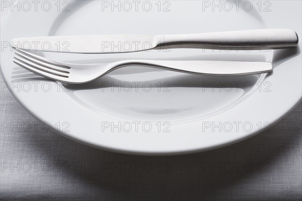 Fork and knife on empty white plate. Photographe : Kristin Lee