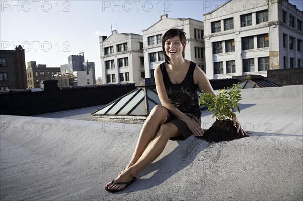 Woman sitting on rooftop beside aspen sapling. Photographe : Shawn O'Connor