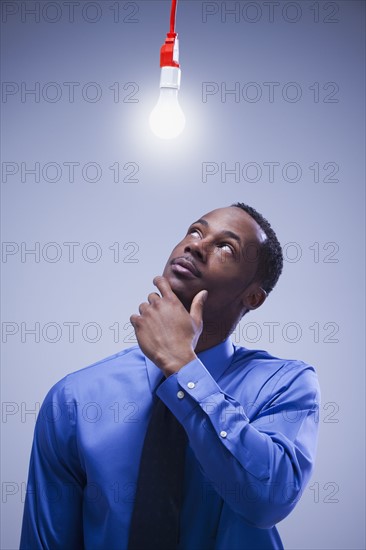 Contemplative businessman standing under a light bulb. Photographe : Mike Kemp