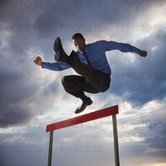 Businessman jumping over a hurdle. Photographe : Mike Kemp