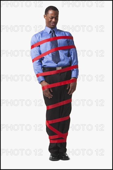 Businessman wrapped in red tape. Photographe : Mike Kemp