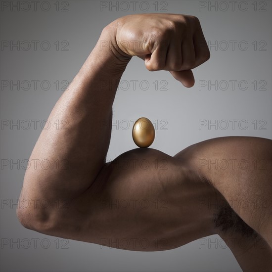 Golden egg perched on a flexed muscular arm. Photographe : Mike Kemp