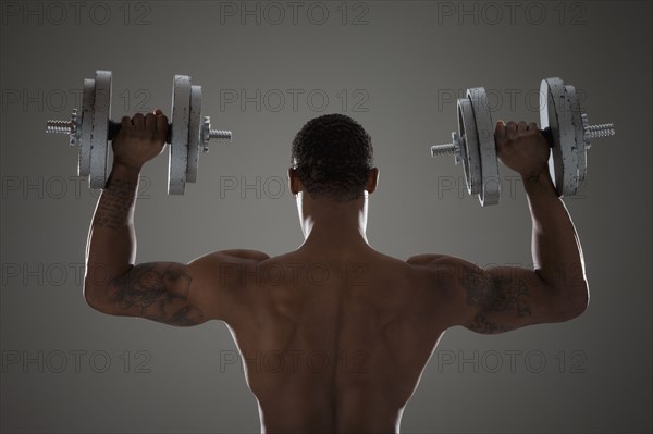 Physically fit man lifting dumbbells. Photographe : Mike Kemp