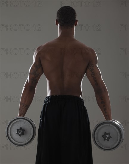 Physically fit man lifting dumbbells. Photographe : Mike Kemp