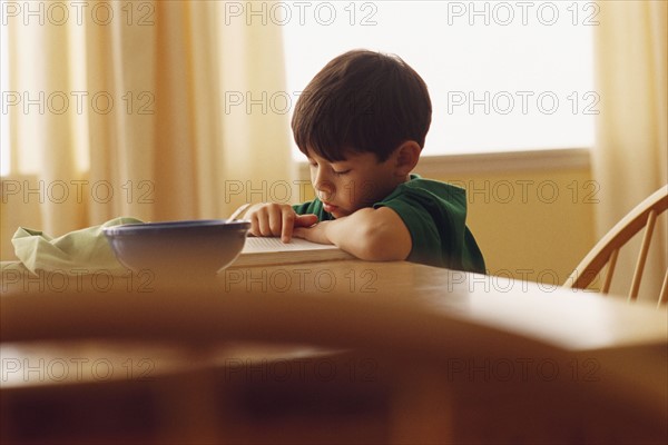 Young boy reading at the kitchen table. Photographe : Rob Lewine