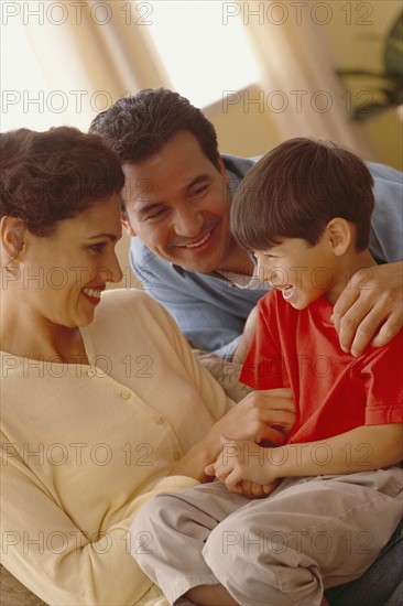 Young boy and his parents relaxing on the couch. Photographe : Rob Lewine
