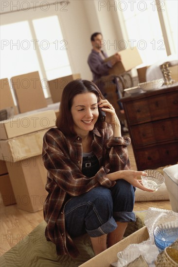 Woman talking on the phone while unpacking boxes. Photographe : Rob Lewine